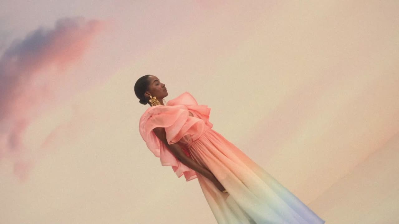 Model in a pink ruffled gown against a pastel sky